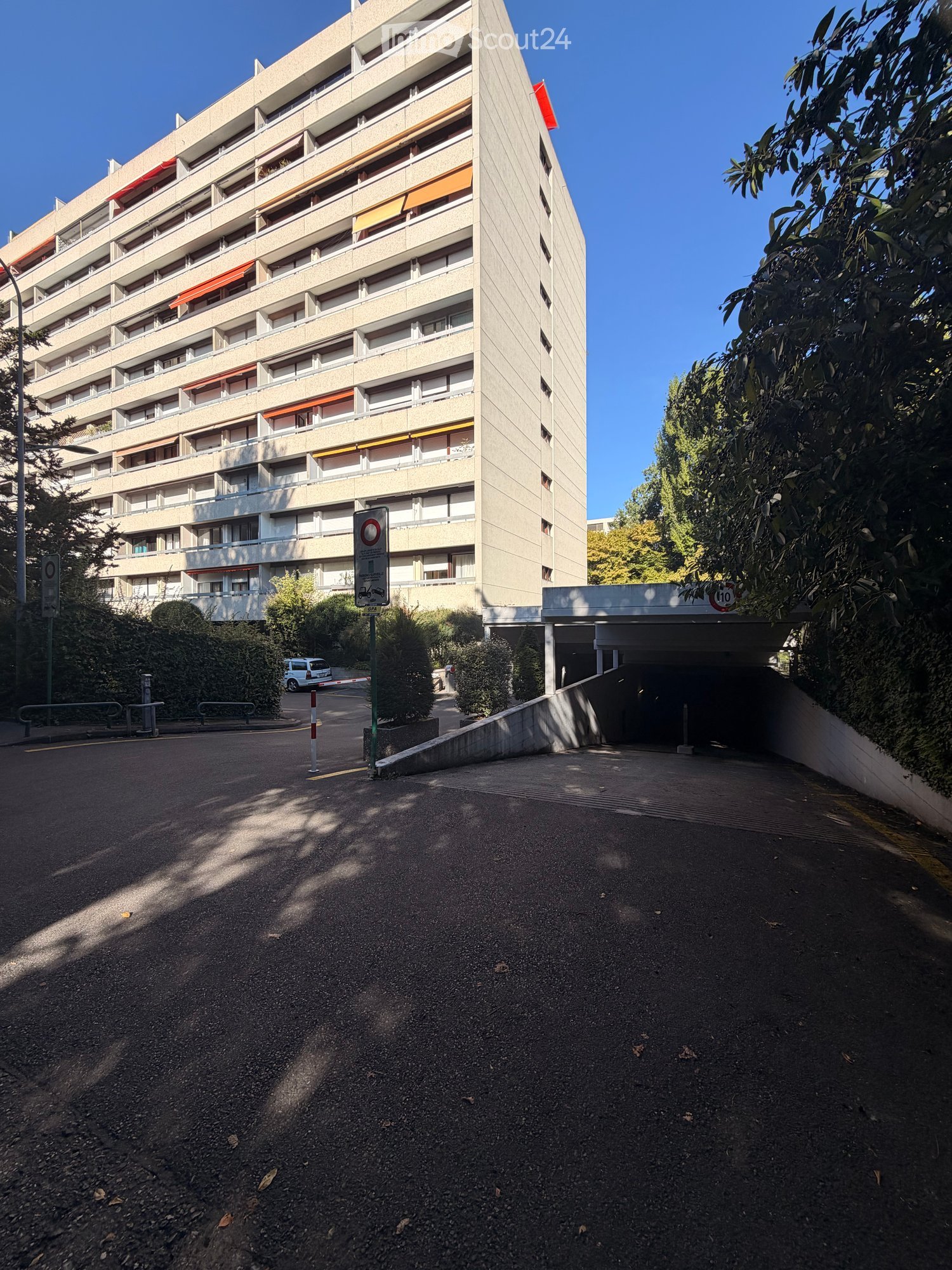 Multi-story residential building with balconies and a covered entrance leading to a parking area.