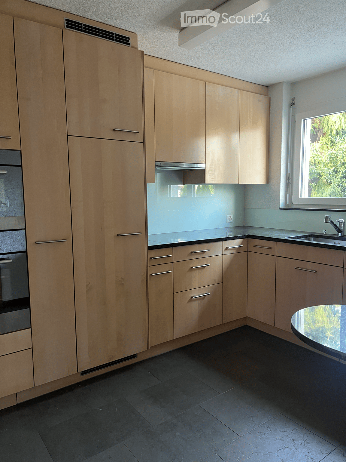 Modern kitchen with light wood cabinets, stainless steel appliances, and a black countertop.