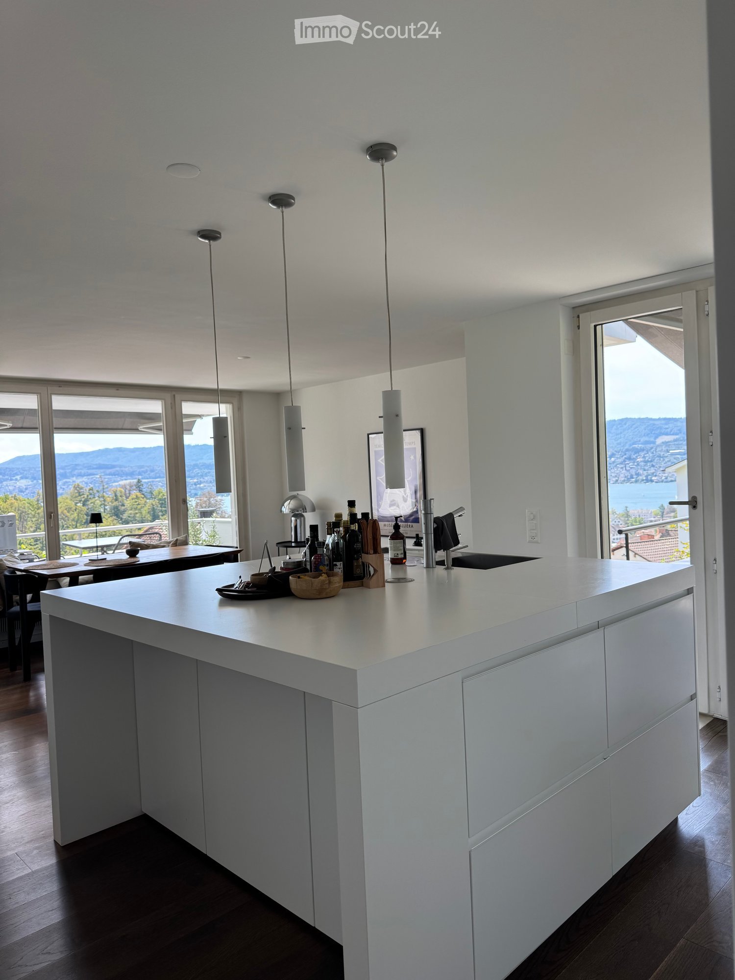 Modern kitchen with a white island, pendant lights, and a view of the lake and mountains through large windows.