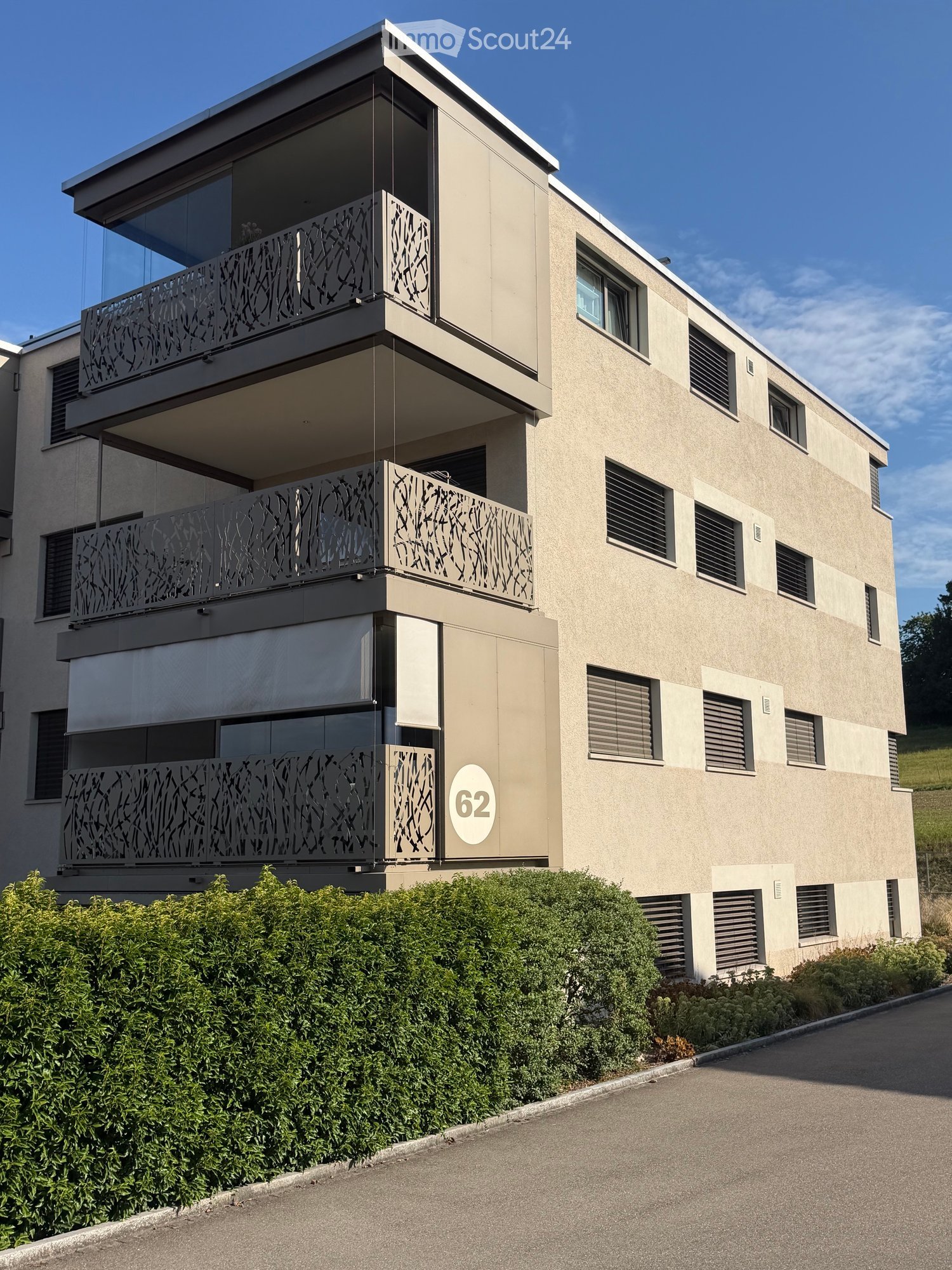 Modern three-story building with beige facade, multiple windows, and decorative metal balconies. The building number "62" is displayed on the front.