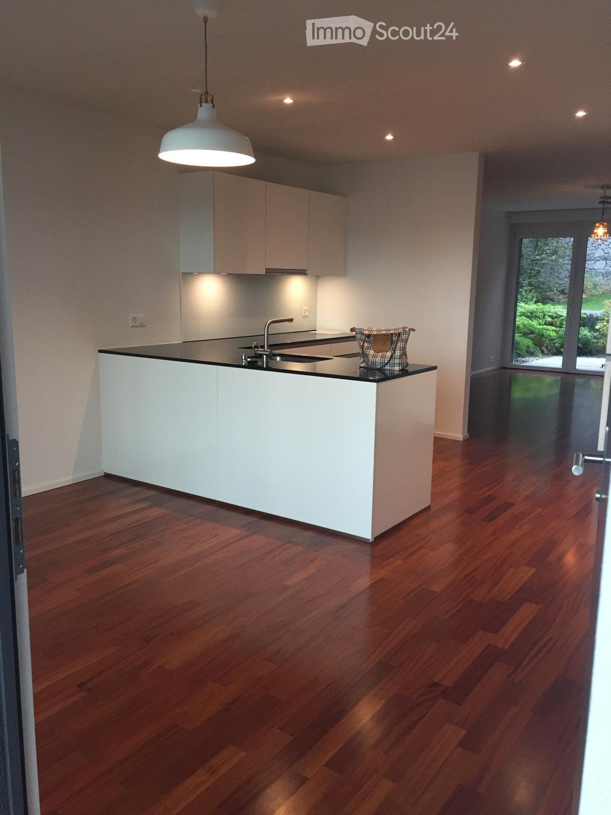 Modern kitchen with white cabinets, a central island, wooden flooring, and a pendant light fixture.