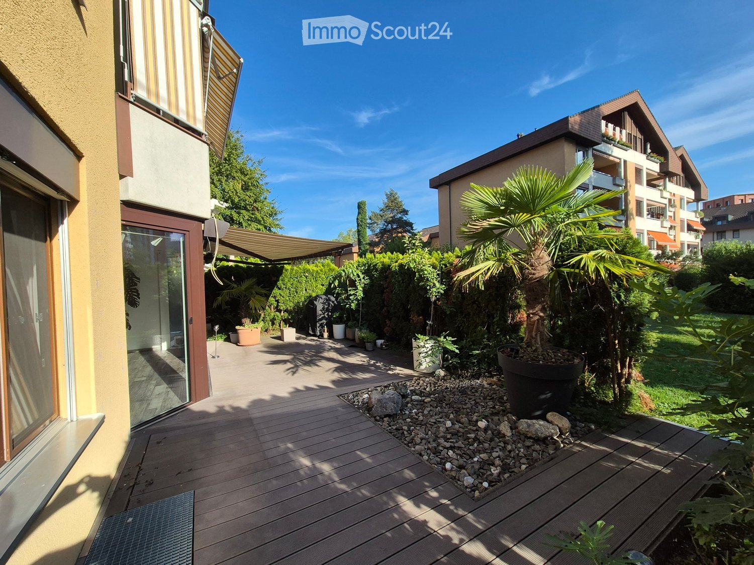 Wooden deck area with potted plants, rocks, and a view of neighboring buildings.
