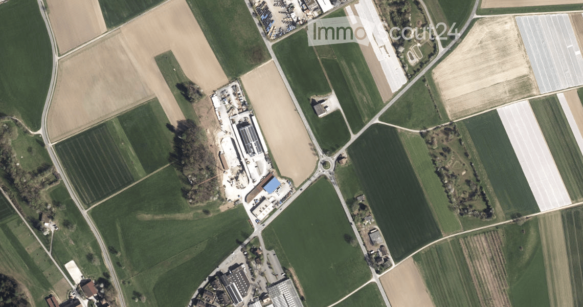 Aerial view of a large industrial building surrounded by agricultural fields and a parking area.