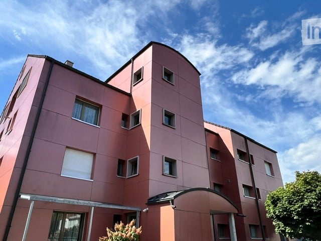 Modern multi-story residential building with pink facade, multiple windows, and a covered entrance area.