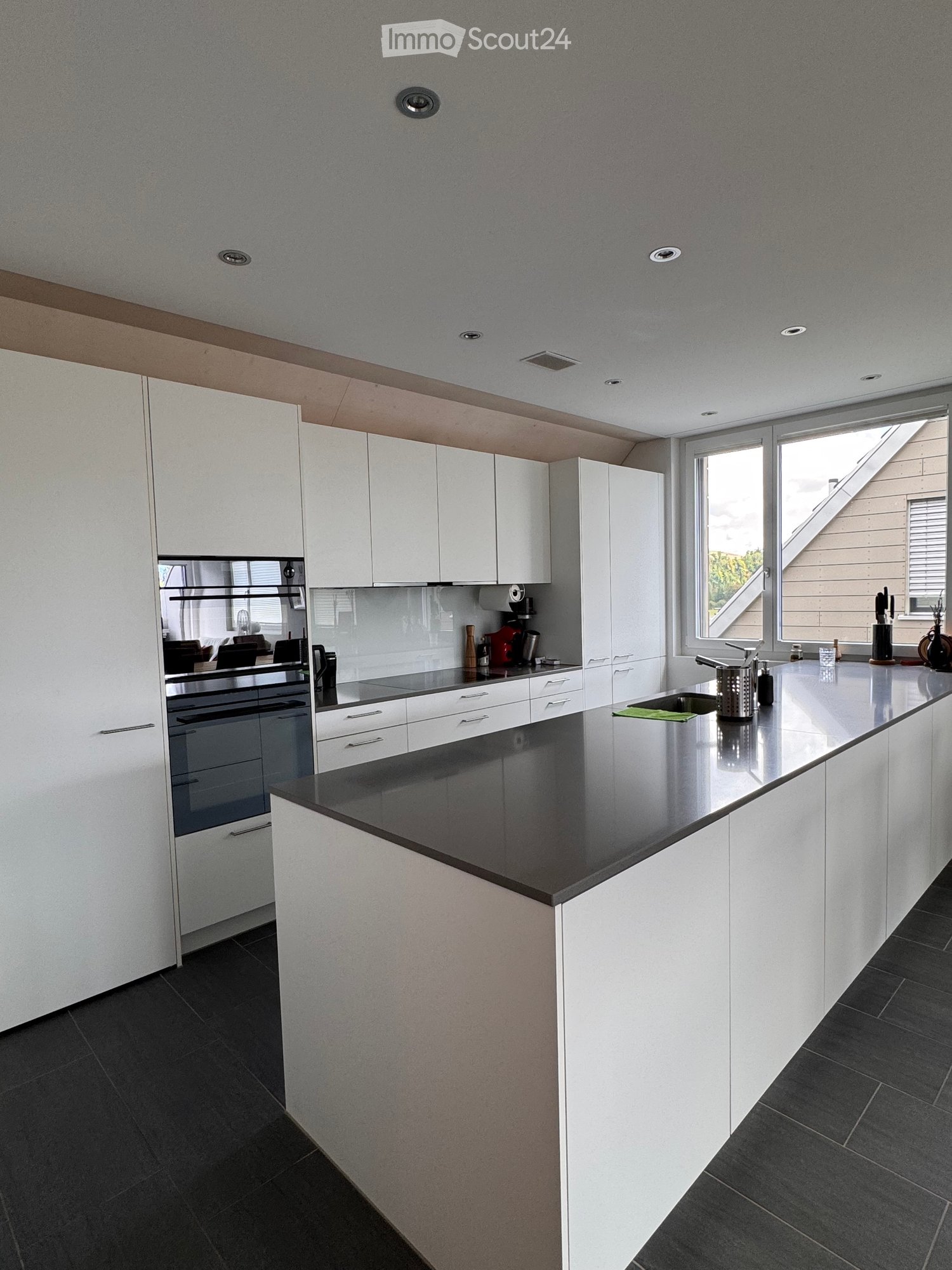 Modern kitchen with white cabinets, dark countertops, and stainless steel appliances. Features a large window and built-in oven.