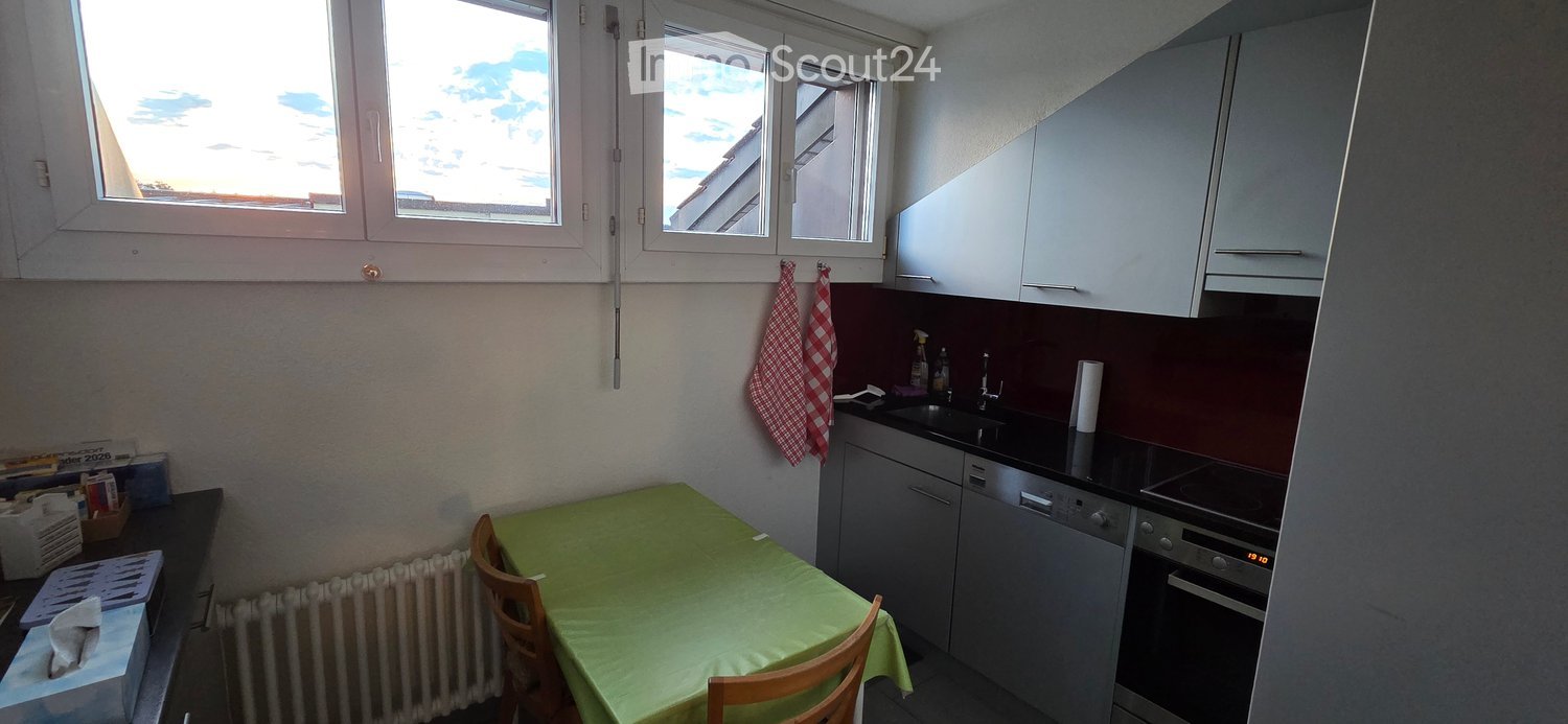 Modern kitchen with white cabinets, black countertops, a dining table with green tablecloth, and two chairs. Includes an oven, dishwasher, sink, and faucet.