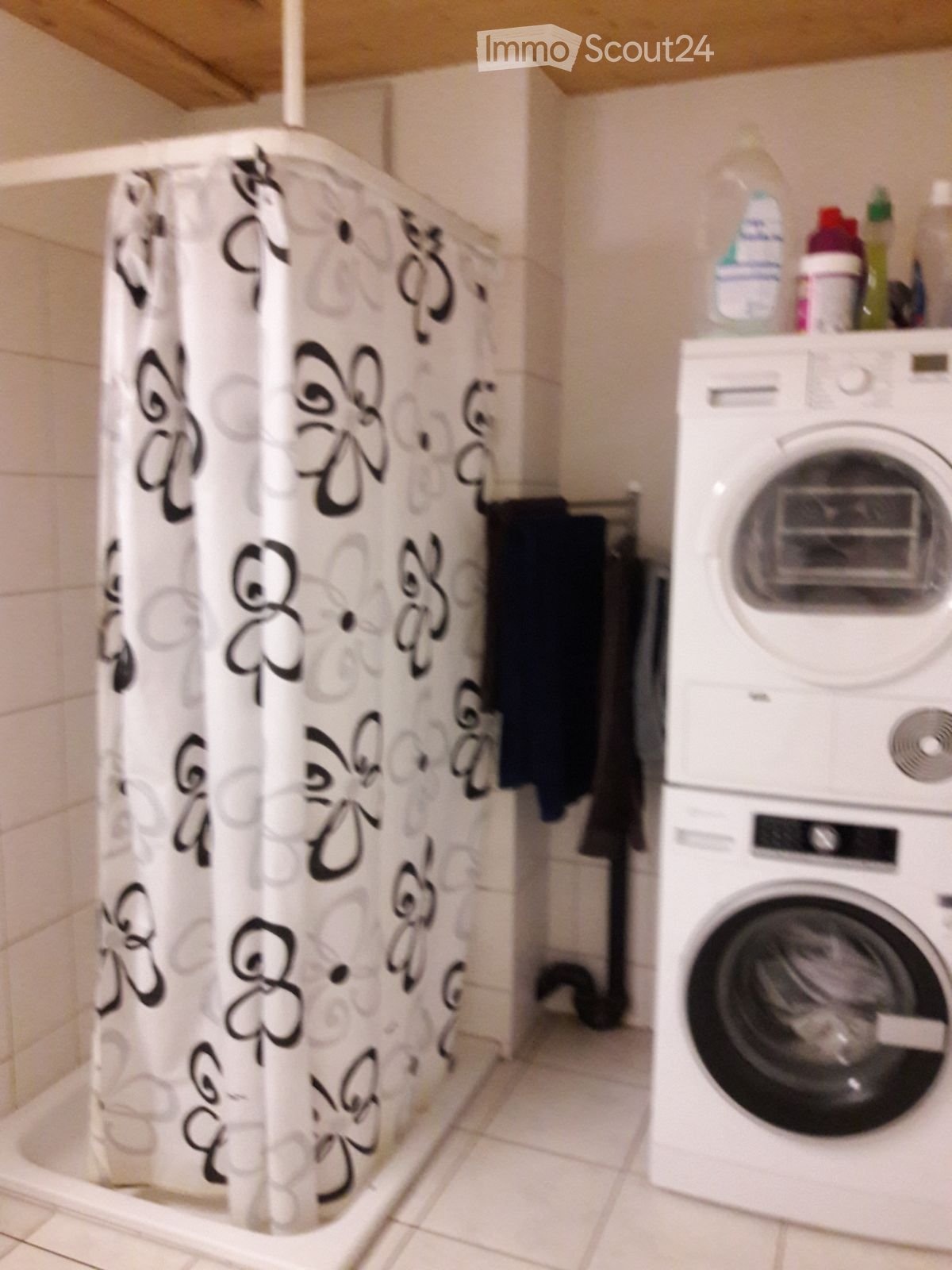 Bathroom with a shower curtain, washing machine, and cleaning supplies on top of the washing machine.