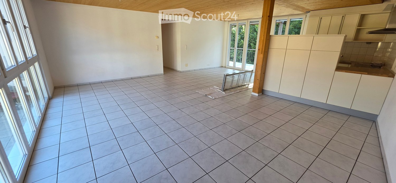 Empty kitchen with tiled floor, white cabinets, and large windows offering a view of greenery. No furniture or appliances are present.