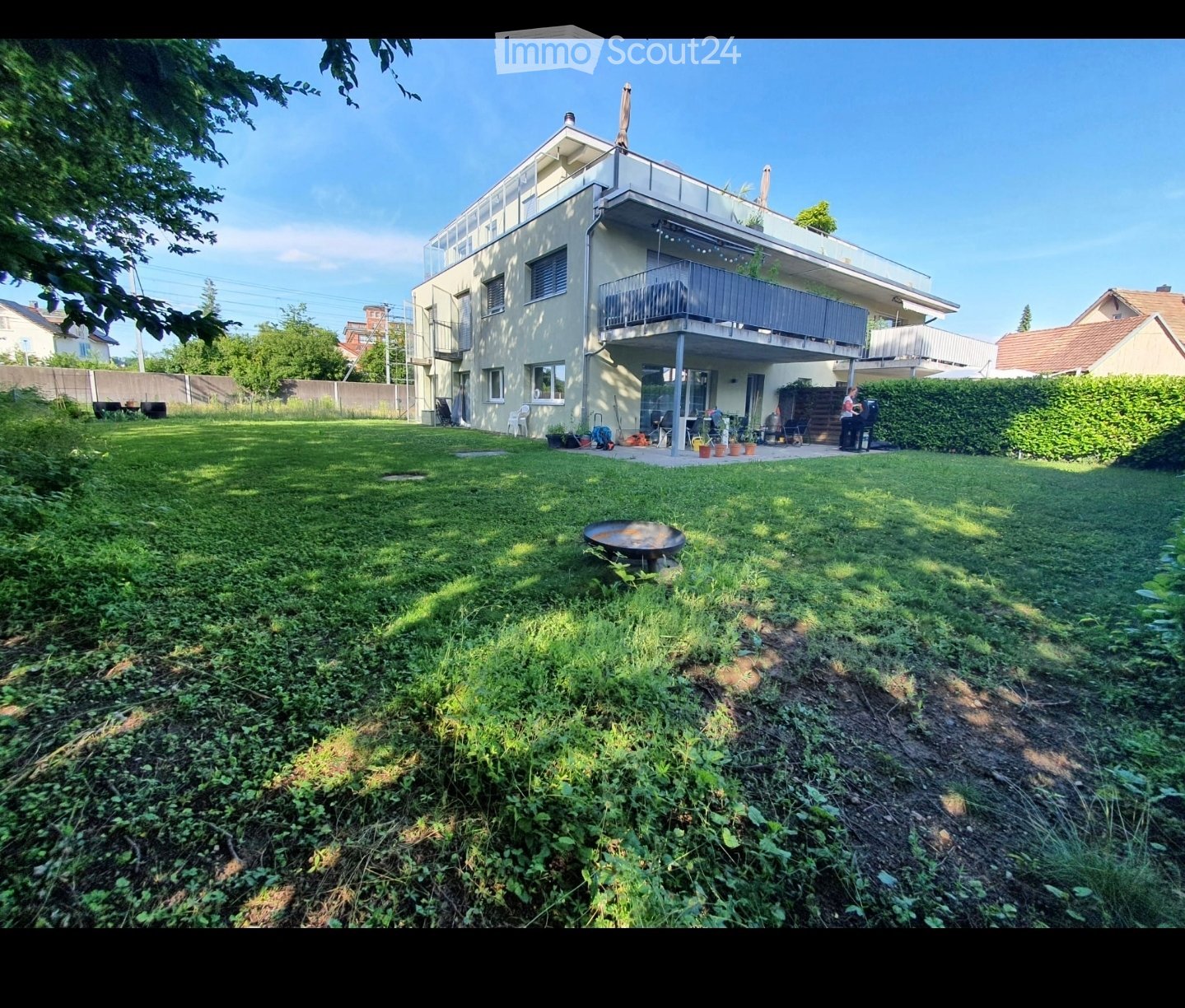 Lush green garden with a barbecue, outdoor seating, and a modern two-story house with balconies and large windows.