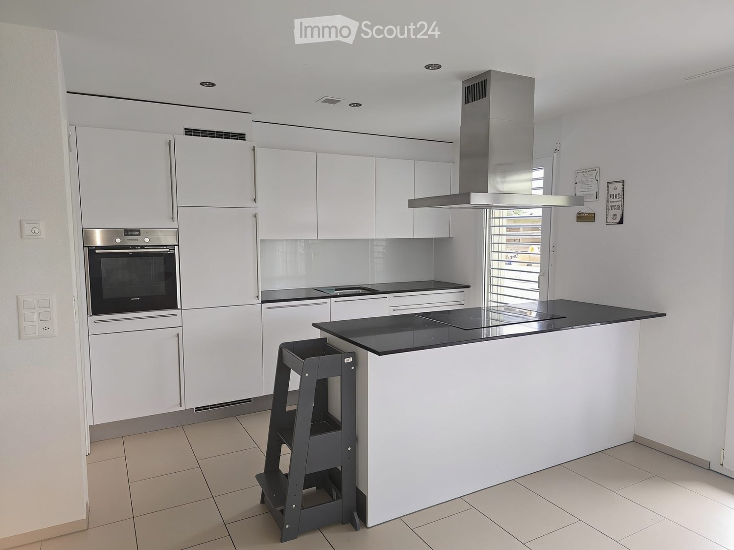 Modern kitchen with white cabinets, stainless steel appliances, black countertops, and a central island with a black countertop and a stool.