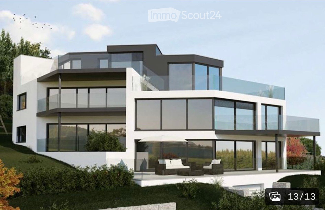 Modern two-story house with large glass windows and balconies, surrounded by greenery and a well-maintained lawn.