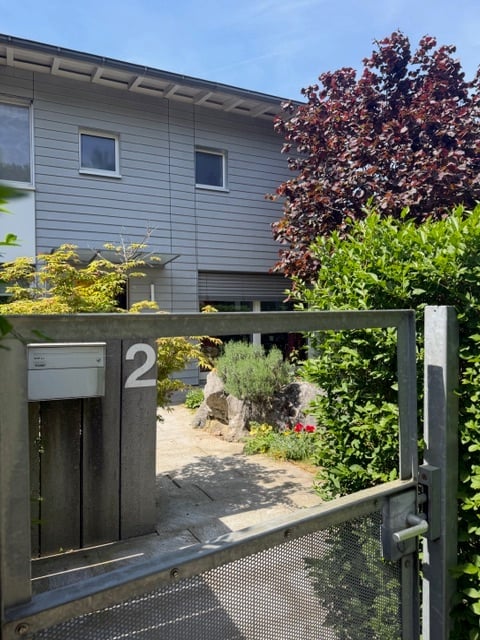 A modern house entrance with a wooden gate displaying the number 2, surrounded by greenery and small plants.