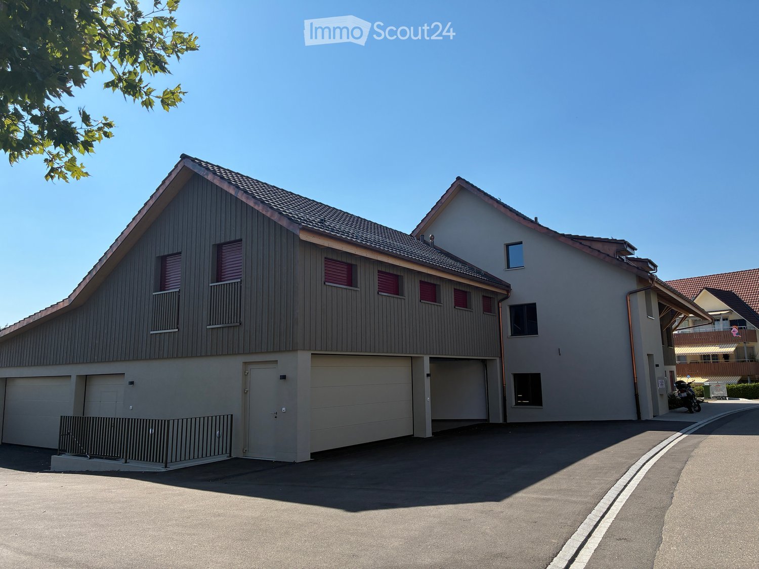 Two-story house with a modern design, featuring a combination of wood siding and plaster walls, multiple garage doors, and a sloped roof with dormer windows.