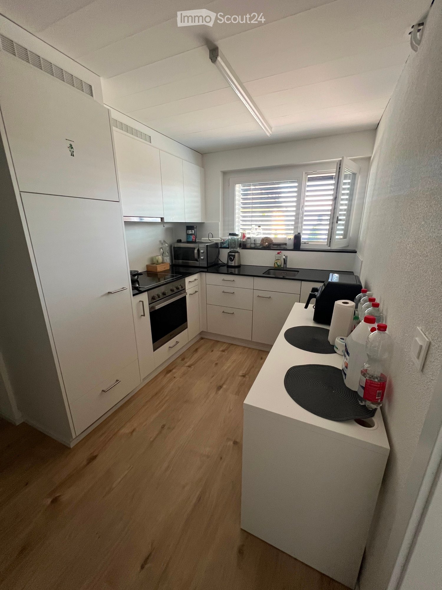 Modern kitchen with white cabinets, wooden flooring, and various appliances including an oven, microwave, and induction cooktop.