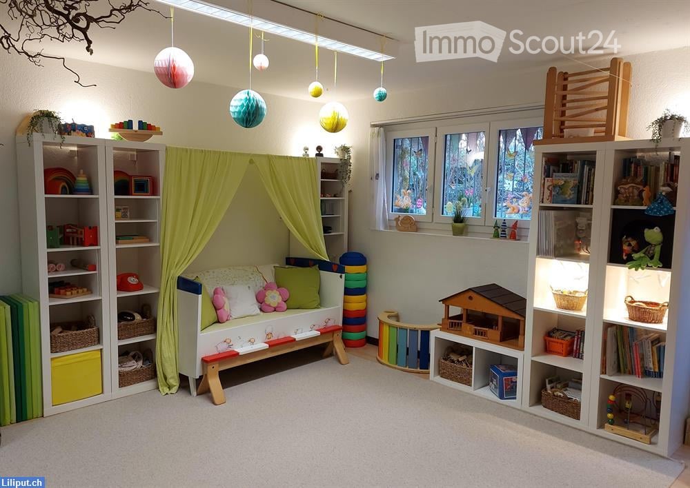 Brightly colored children's room with a small sofa under a green curtain, bookshelves filled with toys and books, a toy house, and colorful storage items.