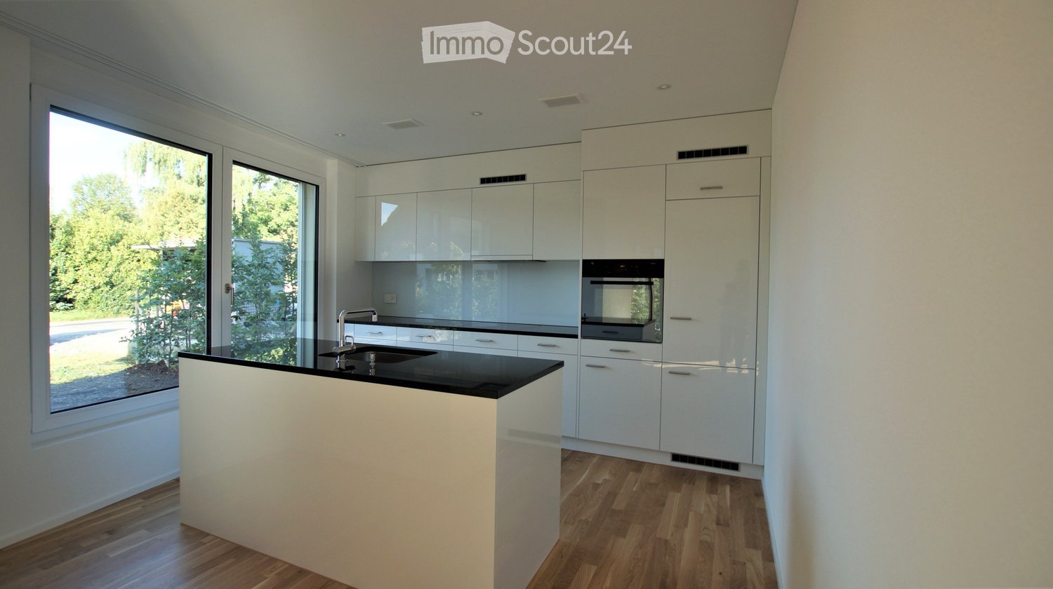 Modern kitchen with white cabinets, black countertop, and a central island. Features a large window with a view of greenery outside.