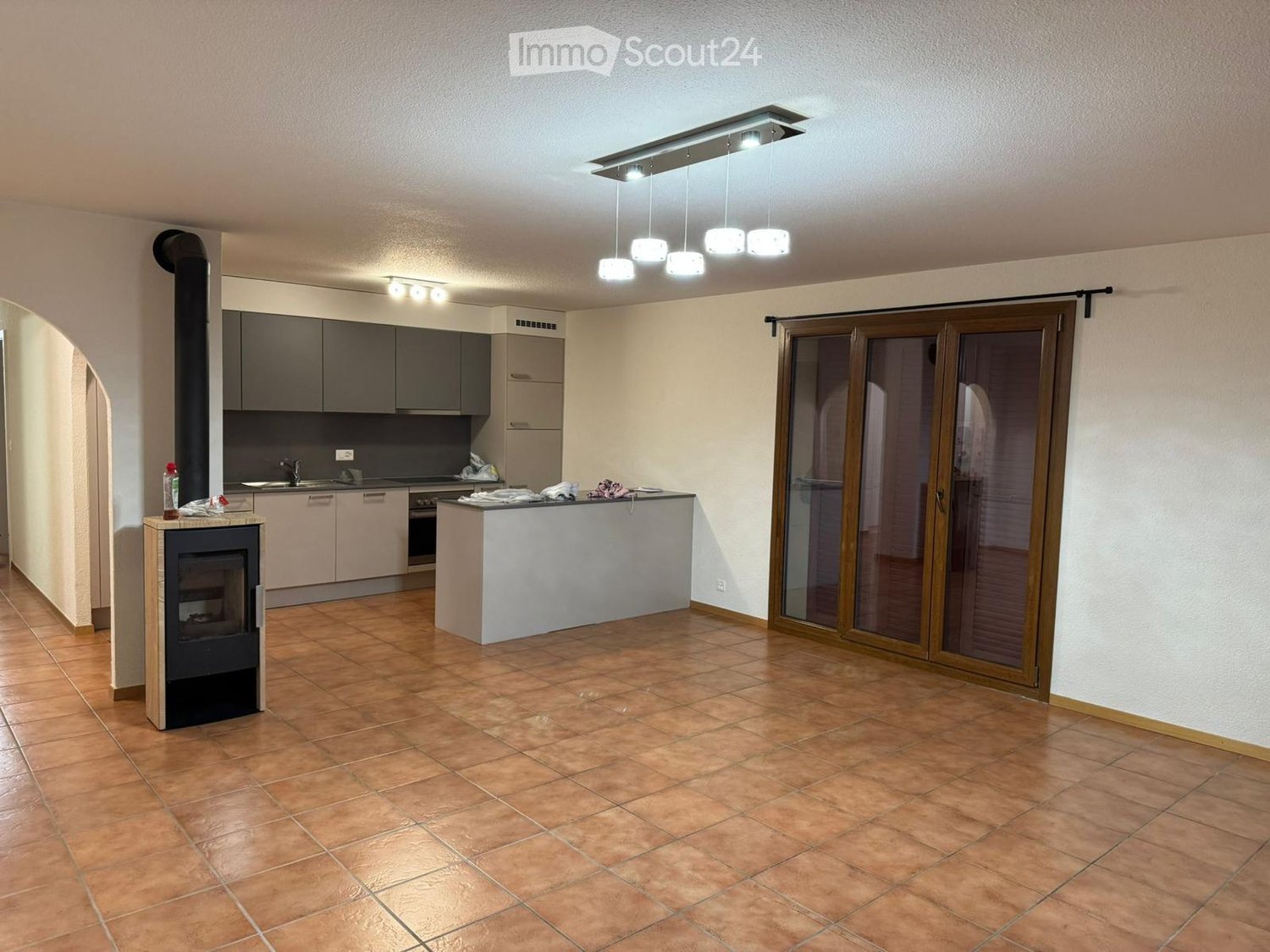 Open-plan kitchen and living area with tiled flooring, modern kitchen cabinets, a central island, and a built-in fireplace.
