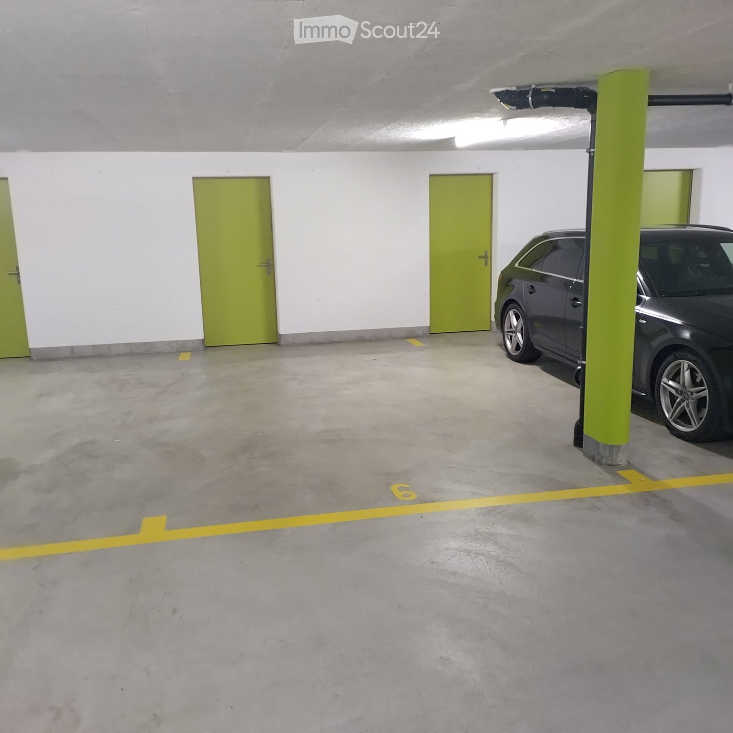 Underground parking area with concrete floors, white walls, green doors, and a parked car.