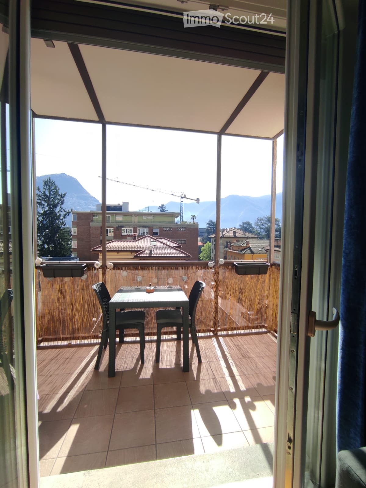 Balcony with a table and two chairs, wooden deck, view of mountains and cityscape.