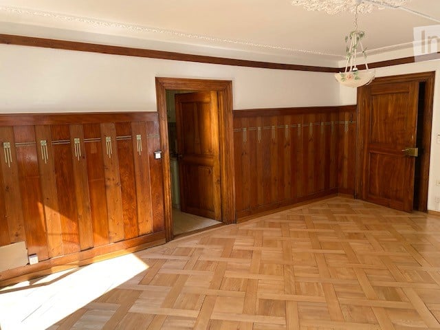 Empty room with wooden panel walls, wooden floor, and two wooden doors.