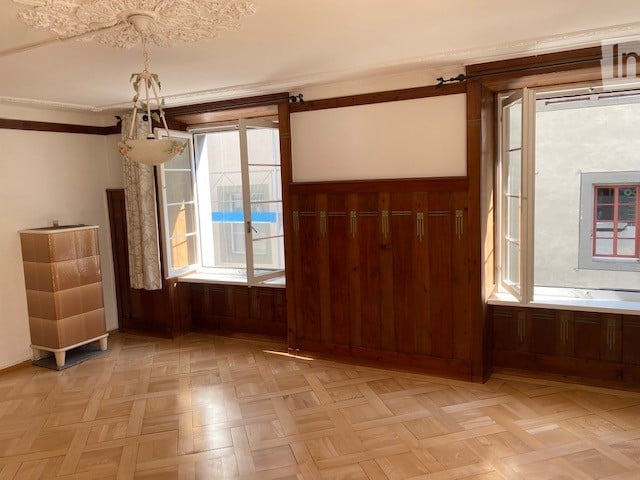 Empty room with wooden flooring, large windows, built-in wooden cabinetry, and a small chest of drawers. No furniture or personal items present.