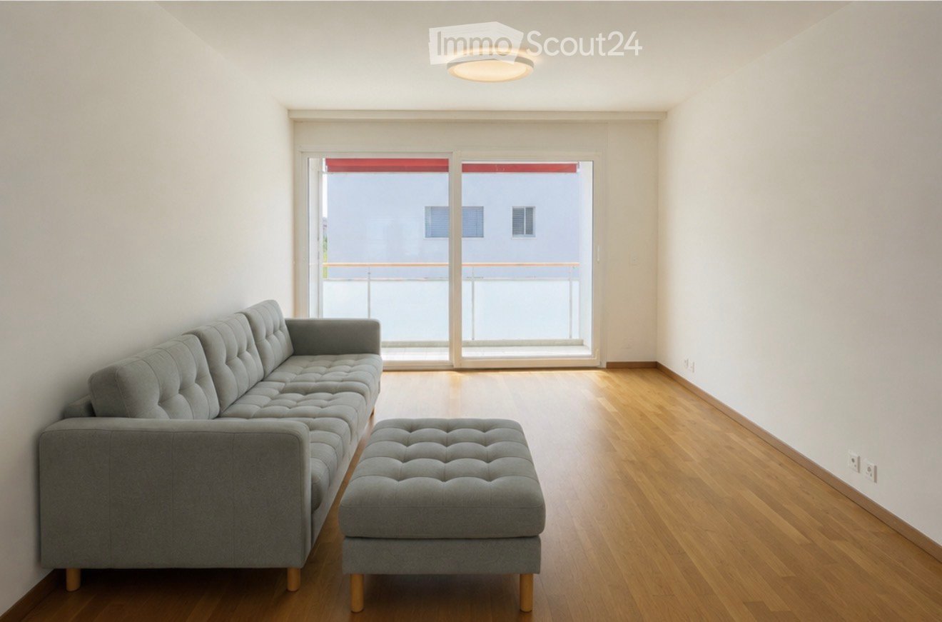 Modern living room with a grey sectional sofa, ottoman, wooden flooring, and large sliding glass doors leading to a balcony.