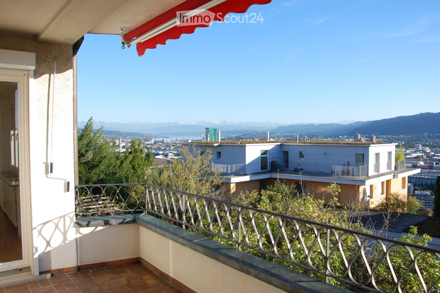 Balcony with a view of a cityscape, mountains, and water, featuring a metal railing and tiled flooring.