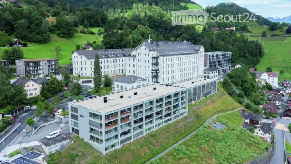 Aerial view of a large, multi-story building complex surrounded by greenery and smaller structures in a rural area.