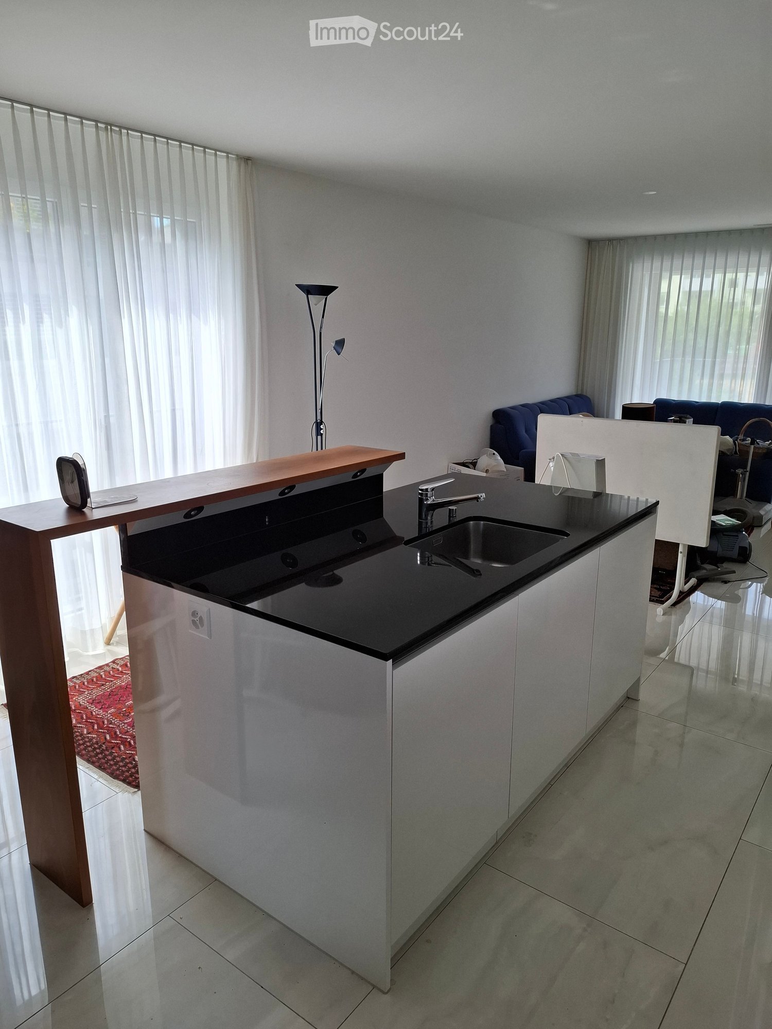 Modern kitchen with white cabinets, black countertop, sink, and a small seating area with a sofa and table.