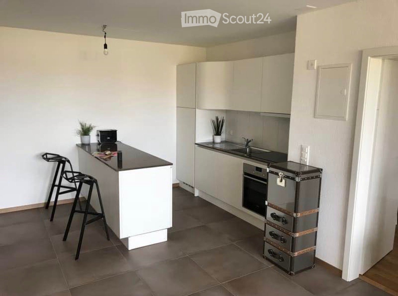 Modern kitchen with white cabinets, dark countertops, a sink, an oven, and a stool near the island.