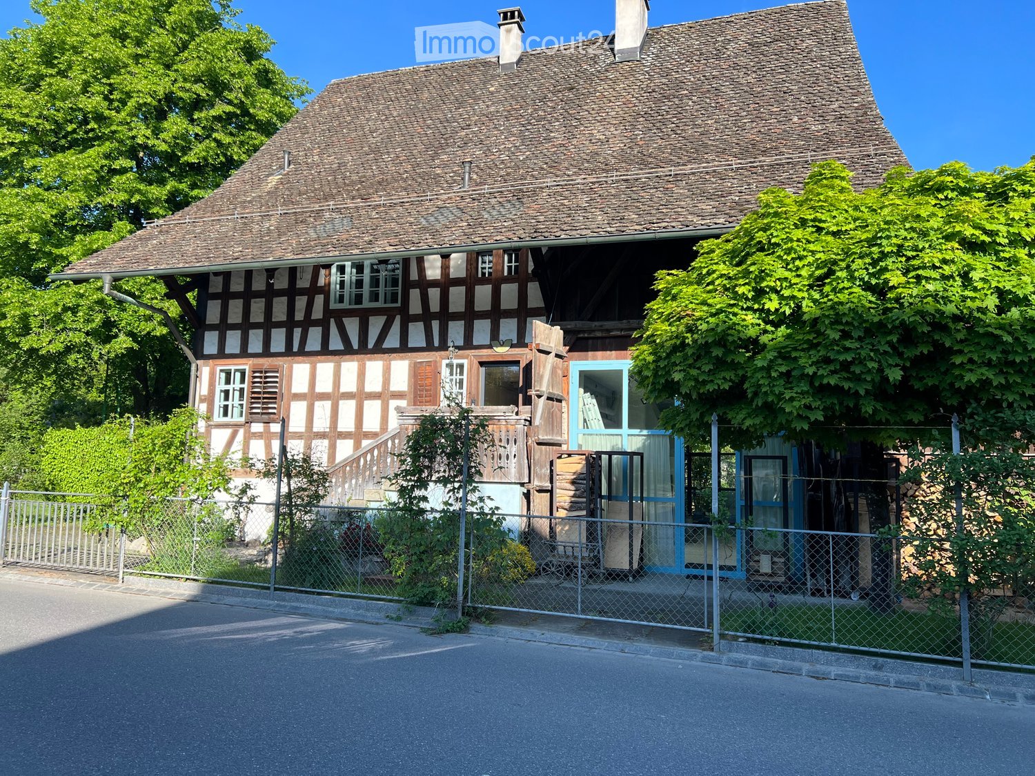 Two-story traditional half-timbered house with a steeply pitched roof, white and brown facade, multiple windows, and a small porch with a staircase leading to the entrance.
