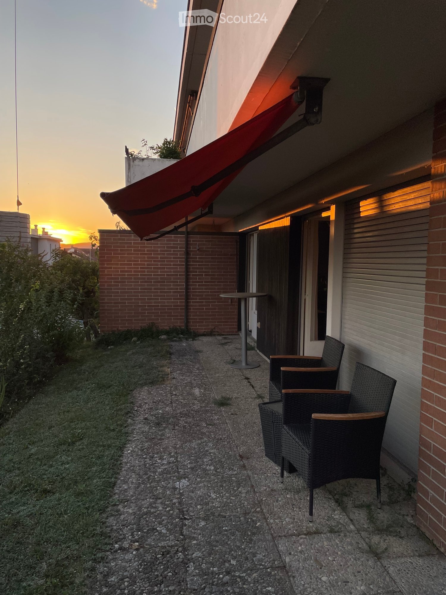 Balcony with a red awning, two wicker chairs, and a small round table.