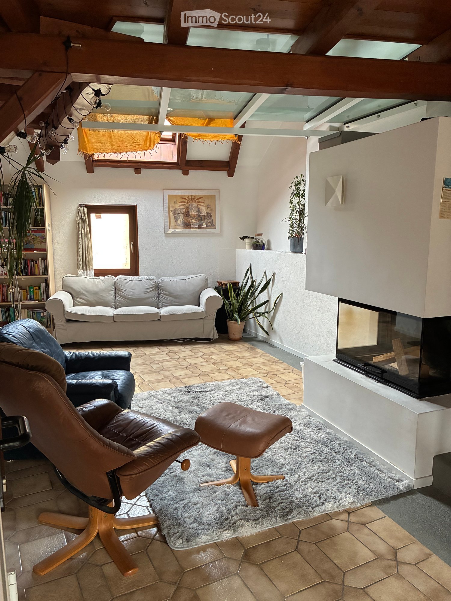 Living room with a white sofa, leather chair, ottoman, fireplace, bookshelf, and plants.