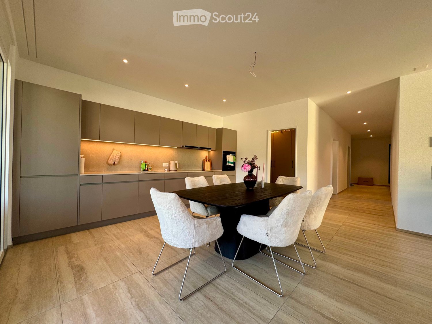 Modern dining area with a dark wooden dining table surrounded by white chairs, grey cabinets, and a vase with flowers on the table.