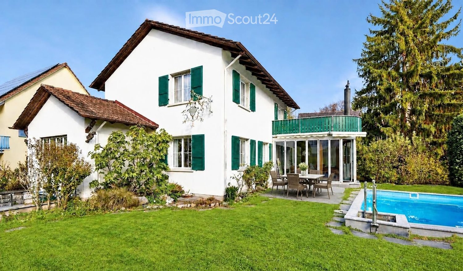 Two-story white house with green shutters, a balcony, a swimming pool, and a well-maintained lawn.