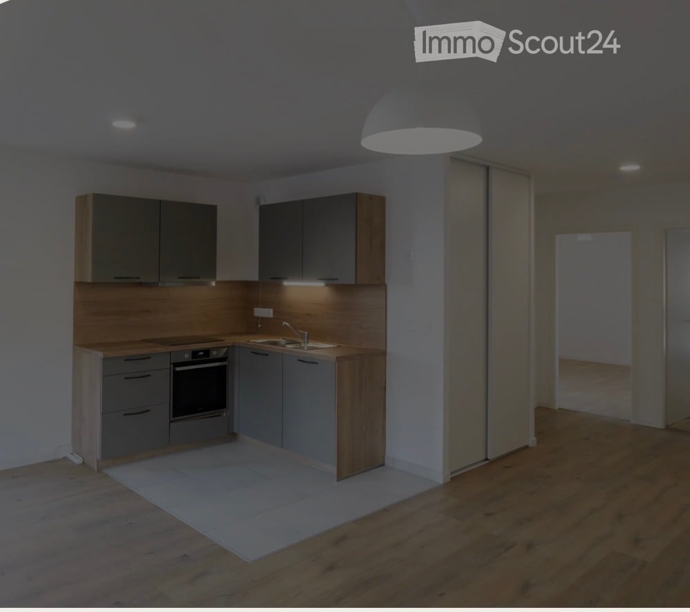 Modern kitchen with grey cabinets, wooden accents, built-in oven, sink, and pendant light. The floor is wooden, and the space is well-lit with under-cabinet lighting.