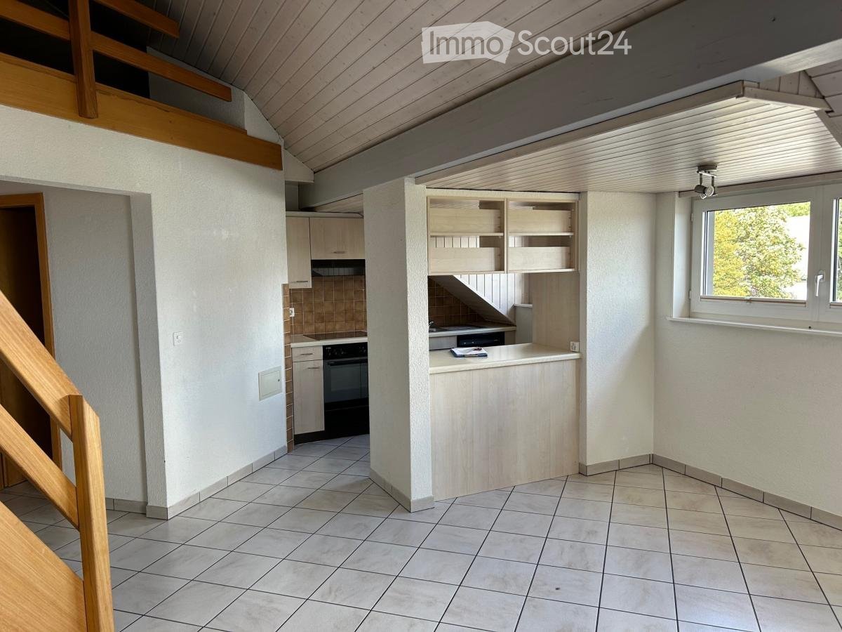 Bright kitchen with tiled floor, white walls, wooden counter, cabinets, and an oven. A staircase leads to an upper level.