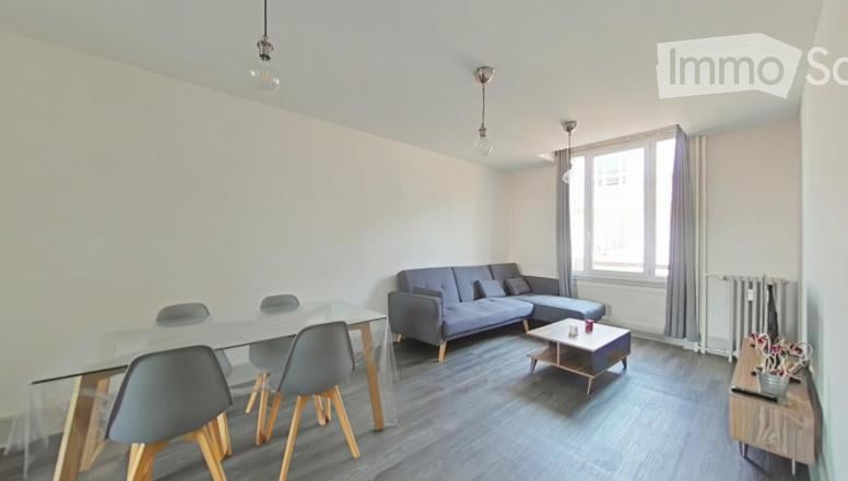 Modern living room with a grey sofa, coffee table, glass dining table, and chairs. Large windows with curtains and pendant lights.