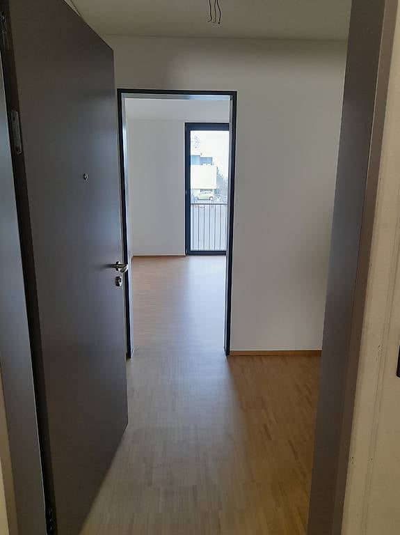 Empty hallway with wooden flooring, leading to a balcony area with a metal railing.