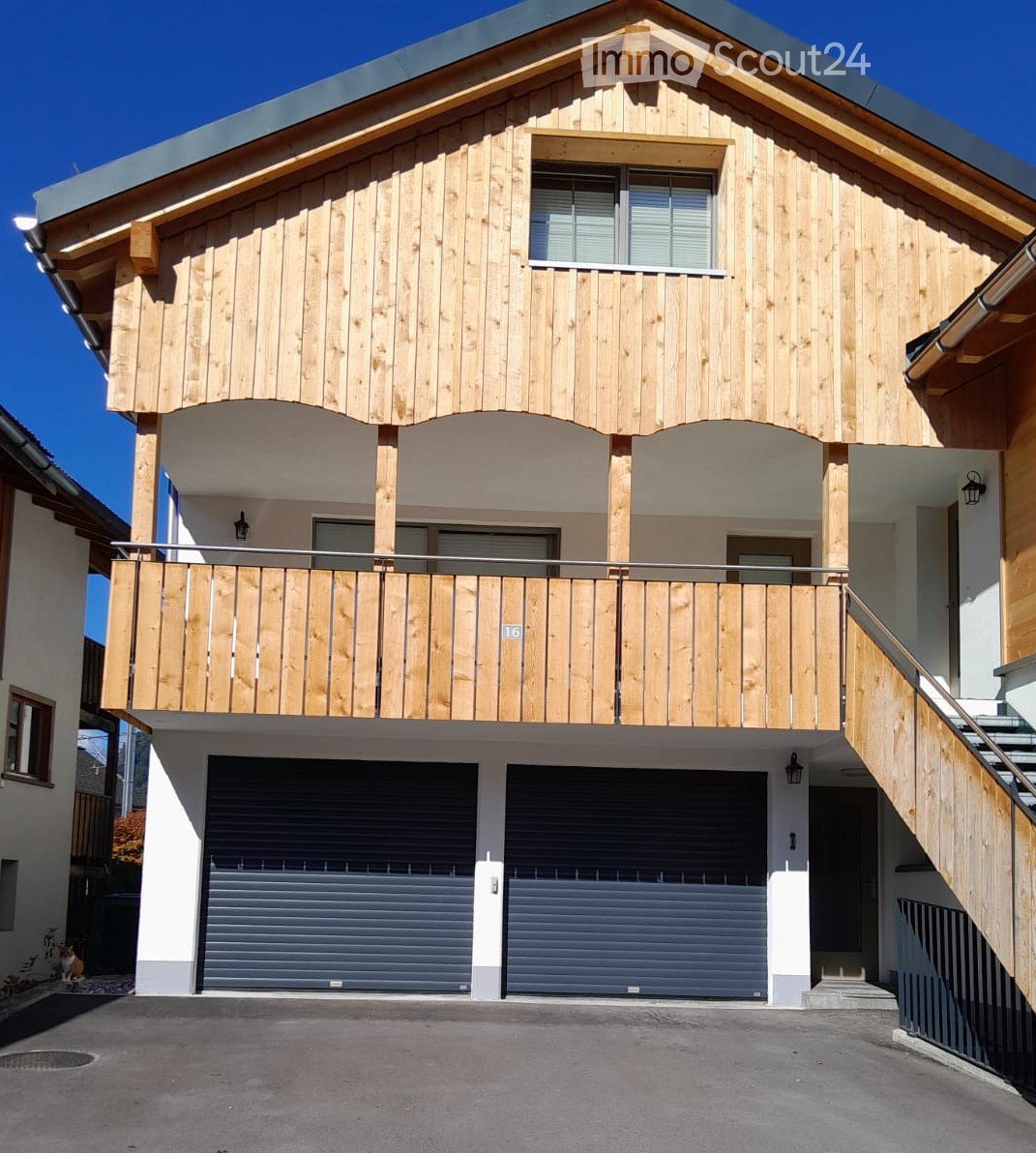 Two-story wooden house with a balcony, garage, and modern design.