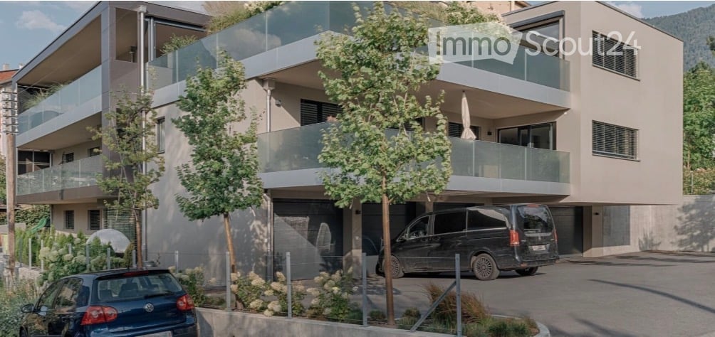Modern multi-story apartment building with balconies, garage, and parking area.