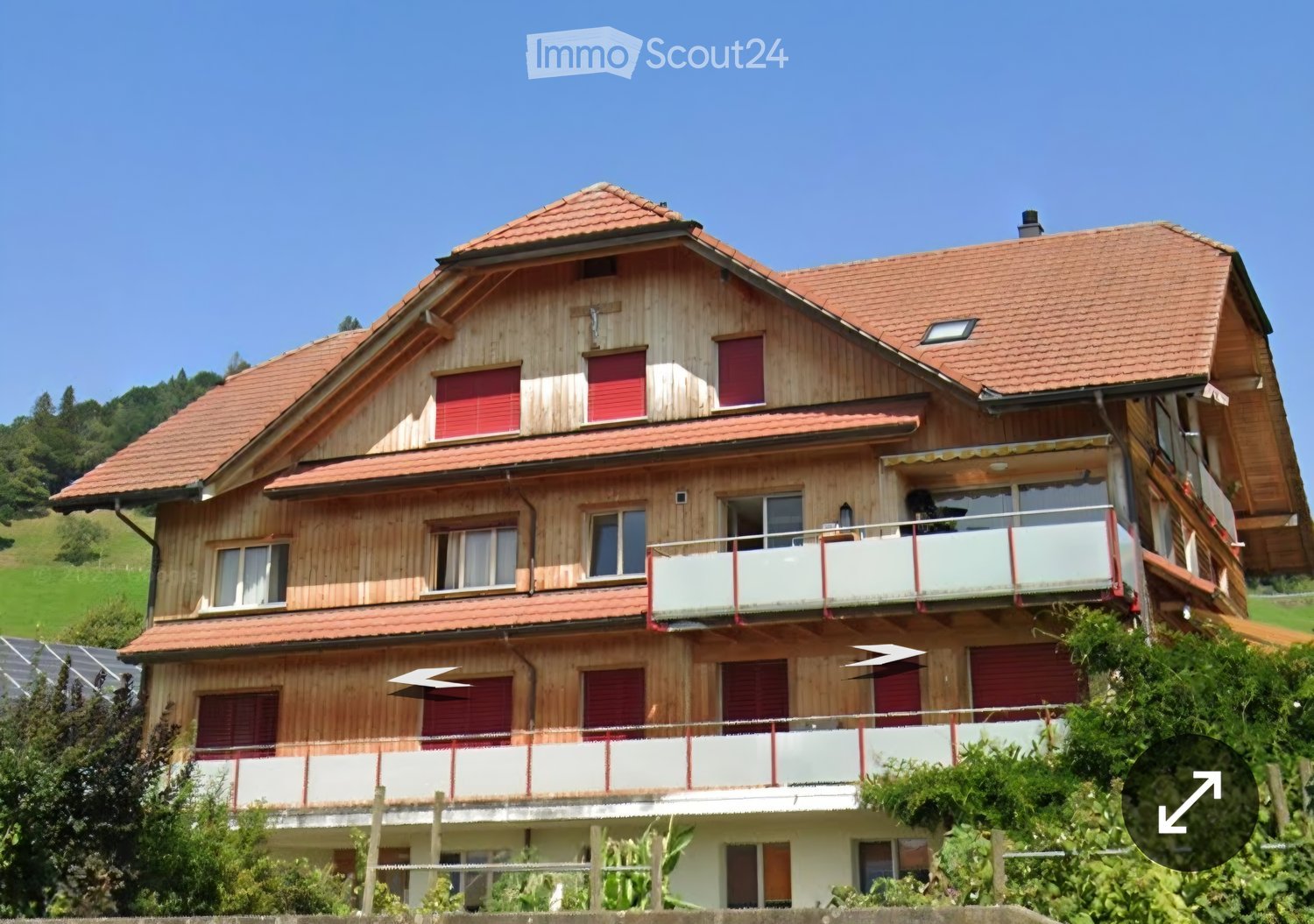Two-story wooden house with red shutters, multiple balconies, and a red-tiled roof.