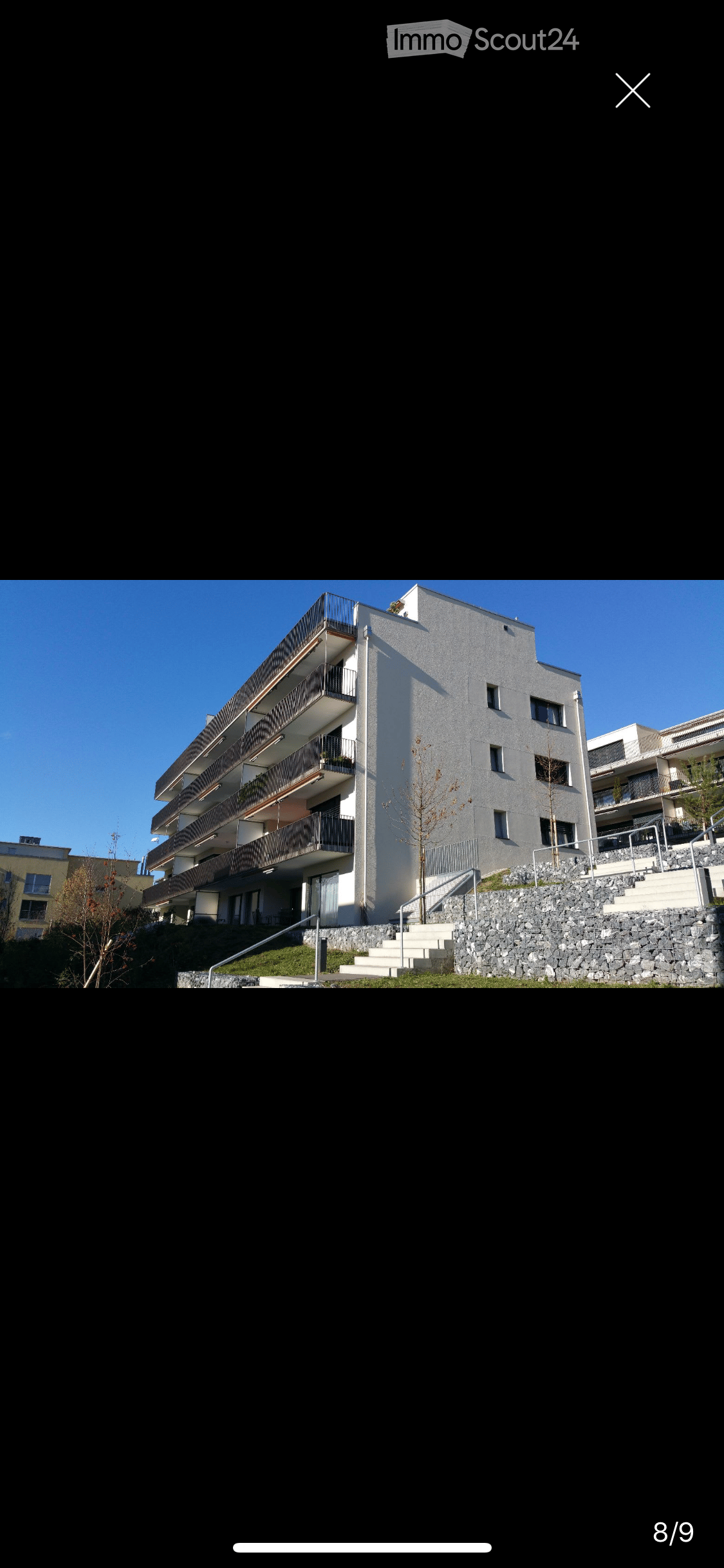 Modern multi-story residential building with balconies, raised ground floor, and stone staircase leading up to the entrance.