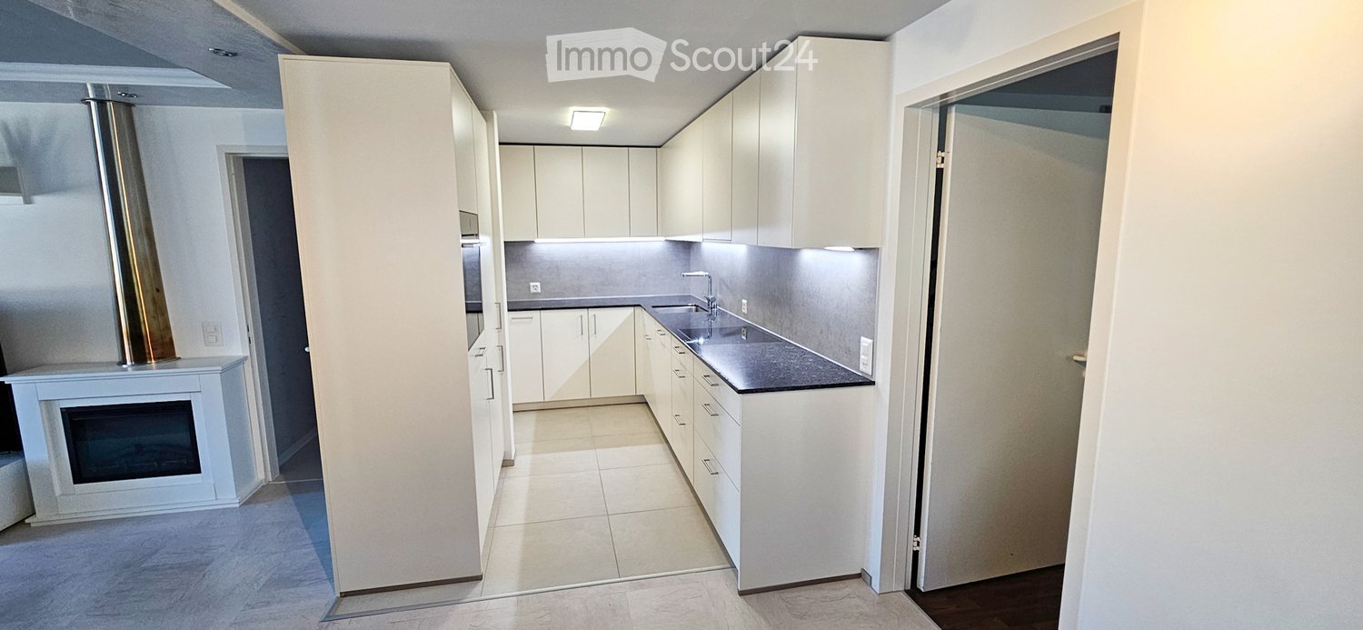 Modern kitchen with white cabinets, black countertop, stainless steel sink, and built-in oven. The space is clean and well-lit with recessed lighting.