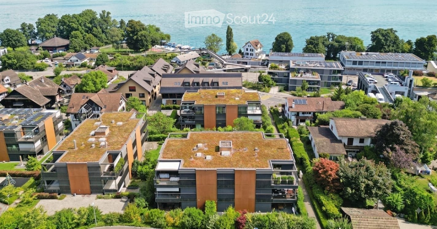Aerial view of a residential area with modern apartment buildings, green roofs, and a scenic lake view in the background.