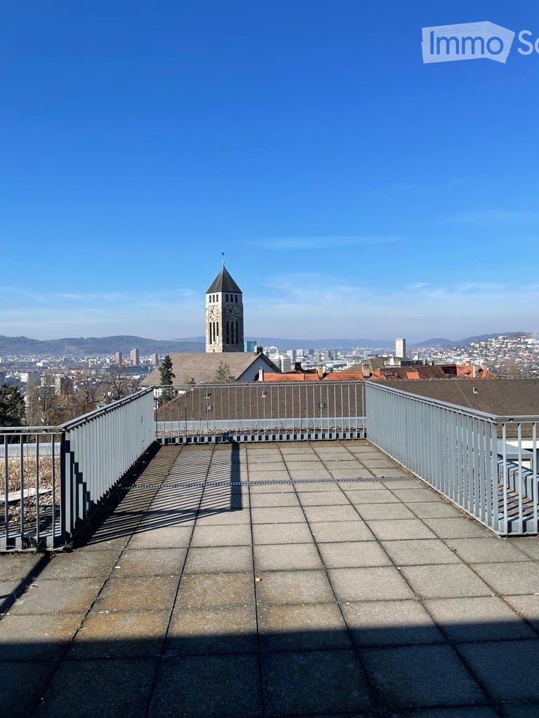 Roof terrace with metal railings, tiled floor, and a panoramic cityscape view including a clock tower and distant buildings.