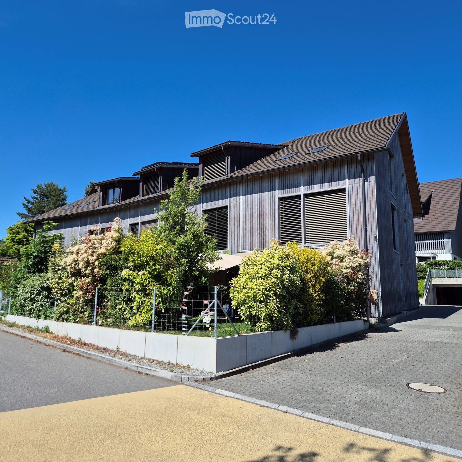 Modern two-story house with wooden exterior, multiple windows, and a fenced garden area.