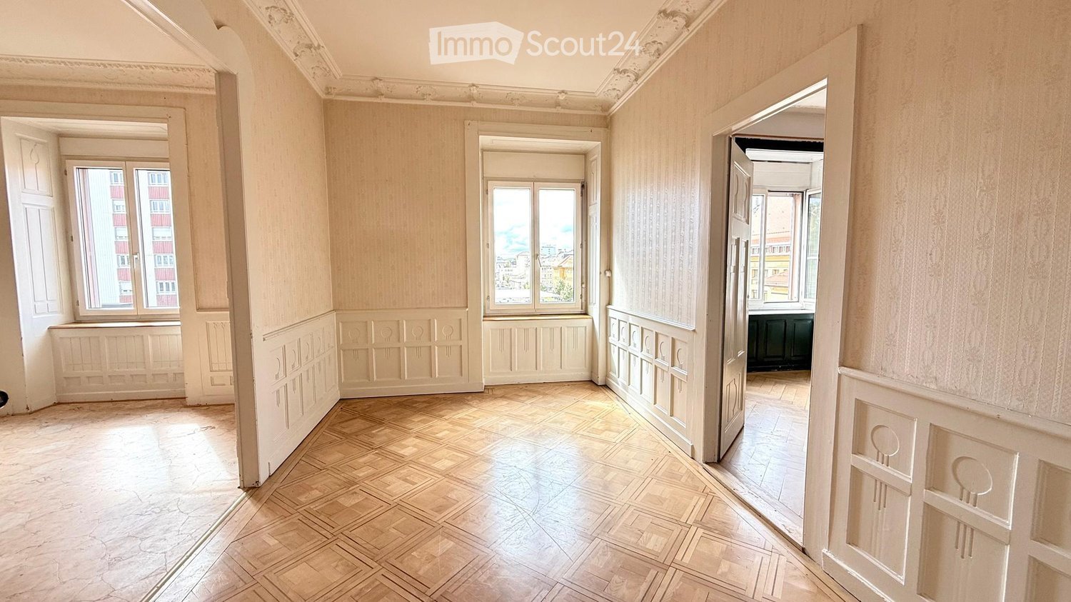 Empty room with light-colored walls, wooden floor, and multiple windows. No furniture or personal items are present.
