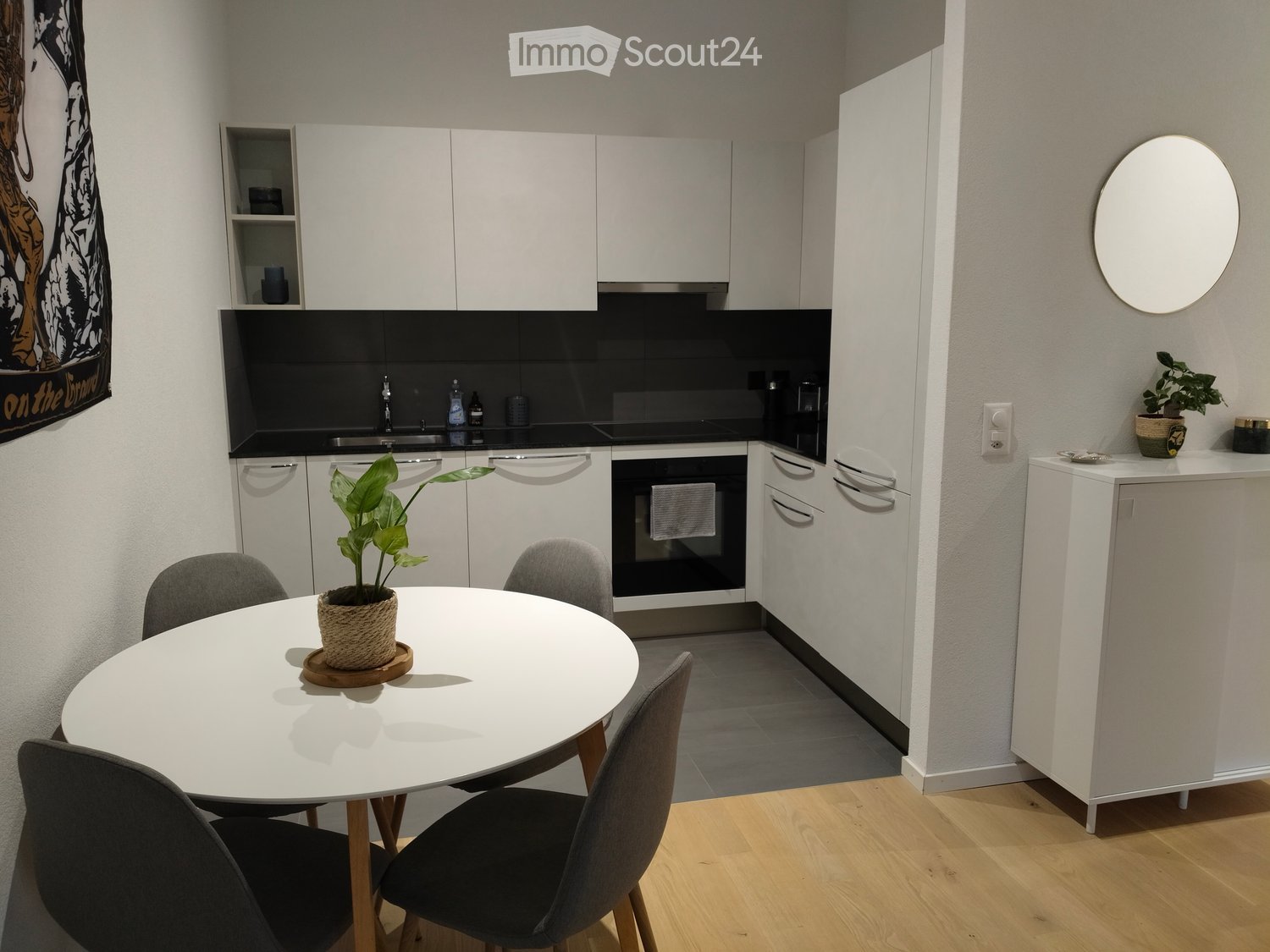 Modern kitchen with white cabinets, a round dining table with four chairs, a potted plant, and a round mirror on the wall.