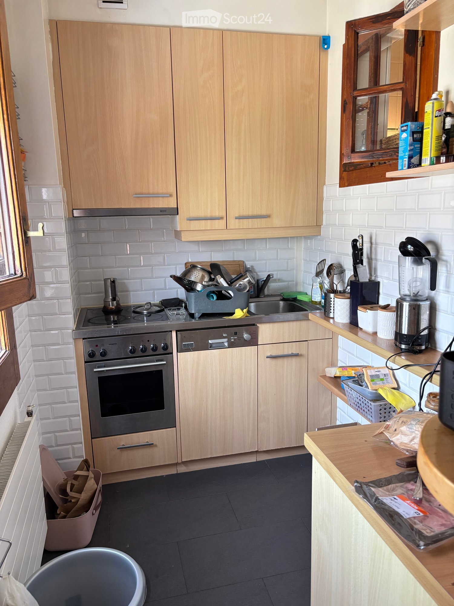 Modern kitchen with light wooden cabinets, stainless steel appliances, and white tiled backsplash. Features an oven, dishwasher, sink, and various kitchen utensils on the counter.
